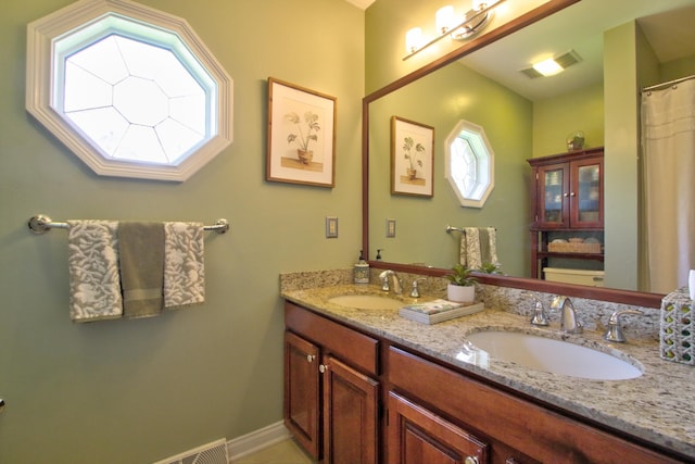 full bath featuring double vanity, a sink, baseboards, and visible vents