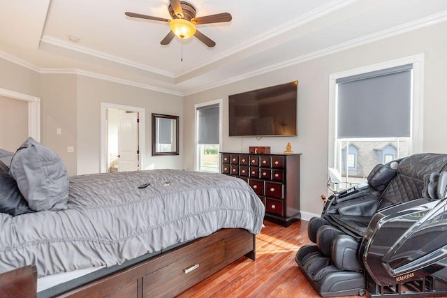 bedroom featuring crown molding, connected bathroom, light wood-style floors, a tray ceiling, and ceiling fan