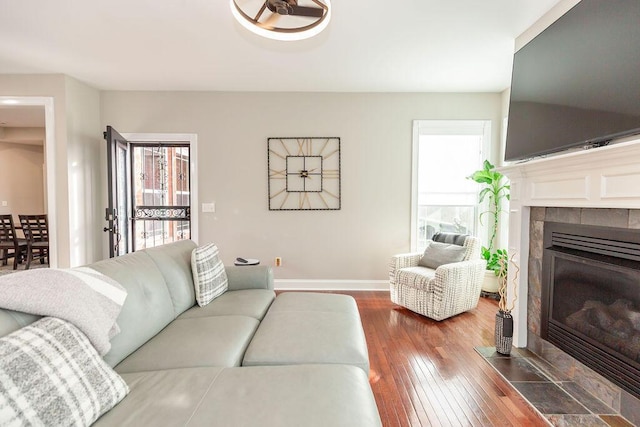 living area with wood-type flooring, baseboards, a tile fireplace, and a healthy amount of sunlight