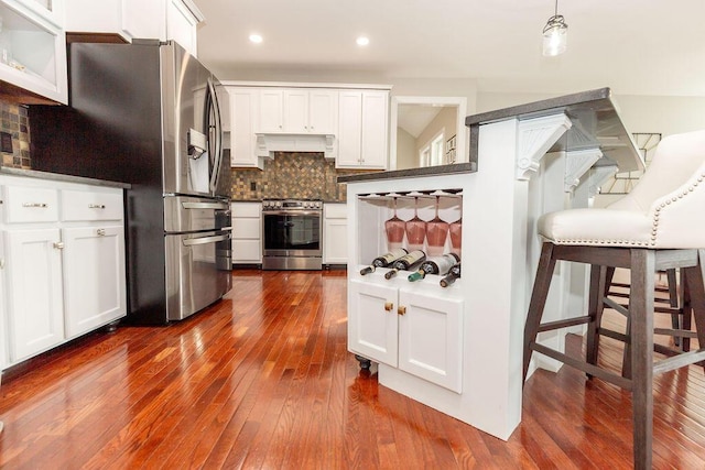 kitchen with tasteful backsplash, custom exhaust hood, white cabinets, appliances with stainless steel finishes, and dark wood-type flooring