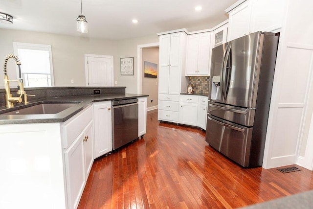 kitchen featuring a sink, dark wood-style flooring, appliances with stainless steel finishes, dark countertops, and backsplash