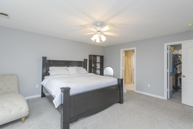 bedroom featuring a walk in closet, baseboards, visible vents, and light colored carpet