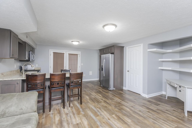 kitchen featuring baseboards, appliances with stainless steel finishes, a textured ceiling, and light wood-type flooring