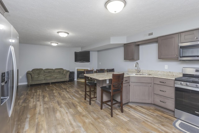 kitchen featuring a sink, open floor plan, a peninsula, appliances with stainless steel finishes, and visible vents