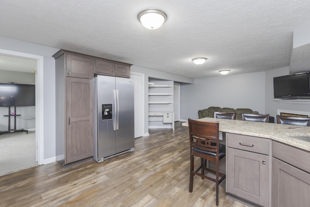 kitchen with light stone counters, a textured ceiling, light wood-style floors, stainless steel fridge with ice dispenser, and built in features