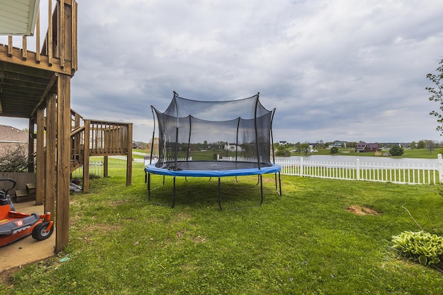 view of yard featuring a trampoline, a deck with water view, stairs, and fence