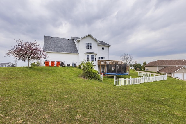 back of property with fence, a lawn, roof with shingles, and a wooden deck