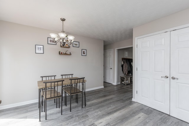 dining area with light wood-type flooring, a textured ceiling, baseboards, and an inviting chandelier
