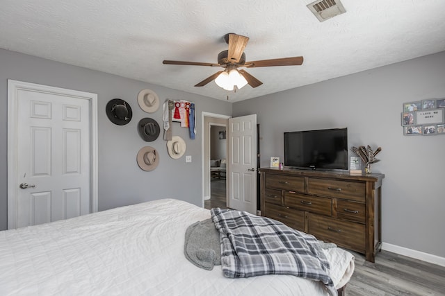 bedroom featuring baseboards, wood finished floors, visible vents, and ceiling fan