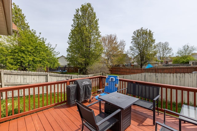 wooden deck featuring a fenced backyard, grilling area, a trampoline, and outdoor dining area