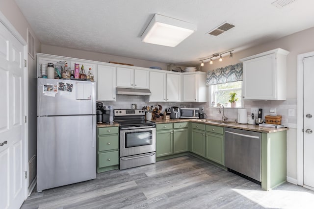 kitchen featuring a sink, green cabinetry, visible vents, under cabinet range hood, and appliances with stainless steel finishes