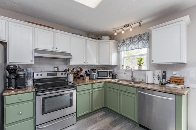 kitchen with white cabinets, stainless steel appliances, a sink, green cabinets, and under cabinet range hood