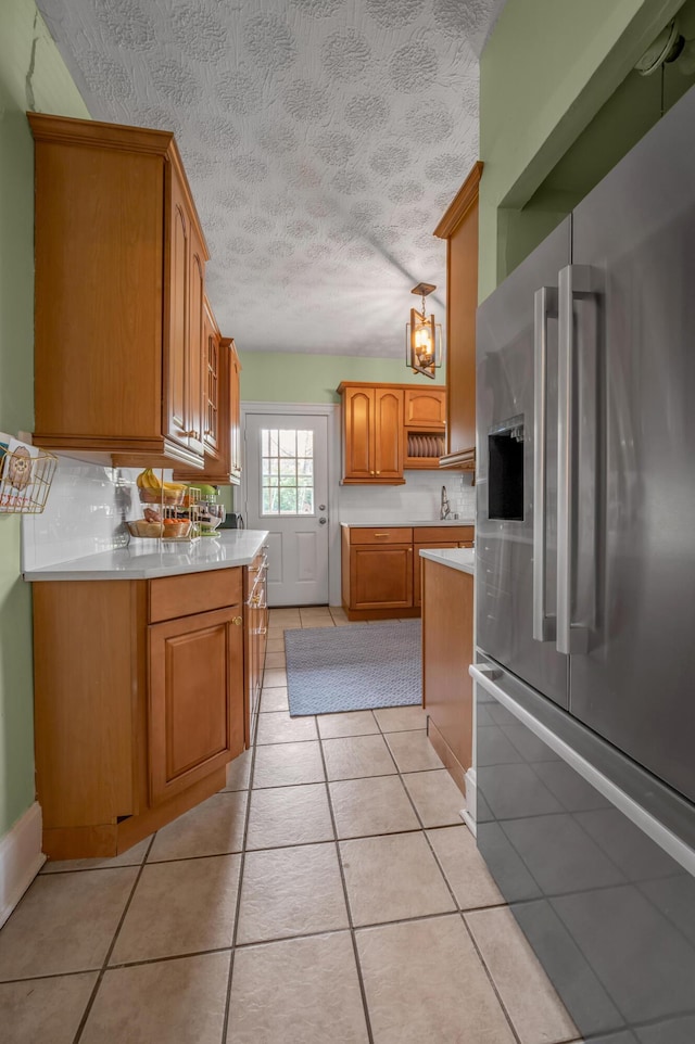 kitchen with stainless steel fridge, a textured ceiling, brown cabinets, light countertops, and light tile patterned floors