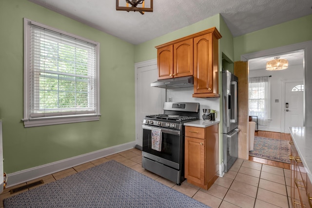 kitchen with under cabinet range hood, visible vents, light tile patterned floors, brown cabinetry, and appliances with stainless steel finishes
