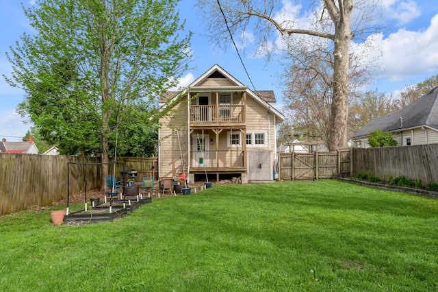 rear view of house with a fenced backyard, a gate, a yard, and a balcony