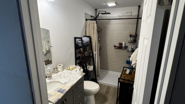 bathroom with toilet, vanity, wood finished floors, and a stall shower