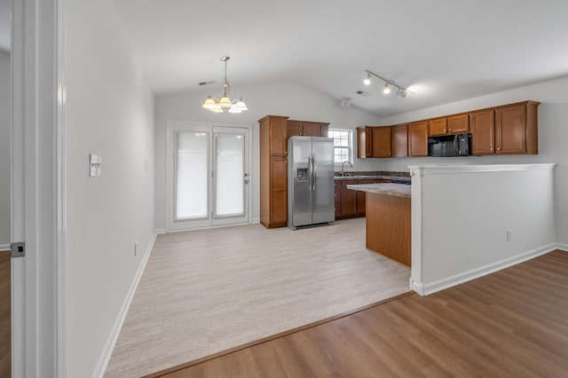 kitchen featuring brown cabinetry, stainless steel fridge, vaulted ceiling, and black microwave