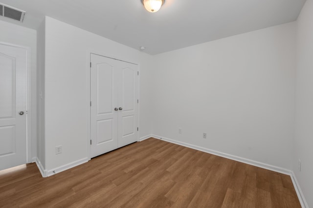 unfurnished bedroom with a closet, visible vents, baseboards, and wood finished floors