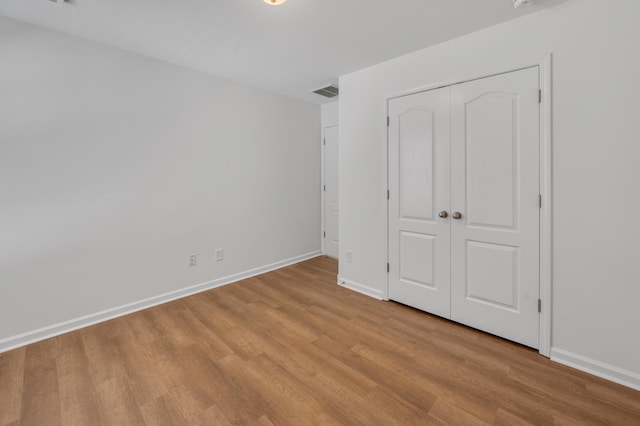 unfurnished bedroom with wood finished floors, baseboards, a closet, and visible vents