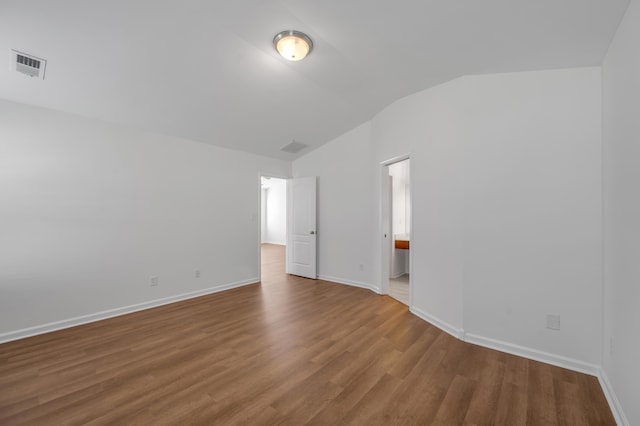 unfurnished room featuring wood finished floors, baseboards, vaulted ceiling, and visible vents