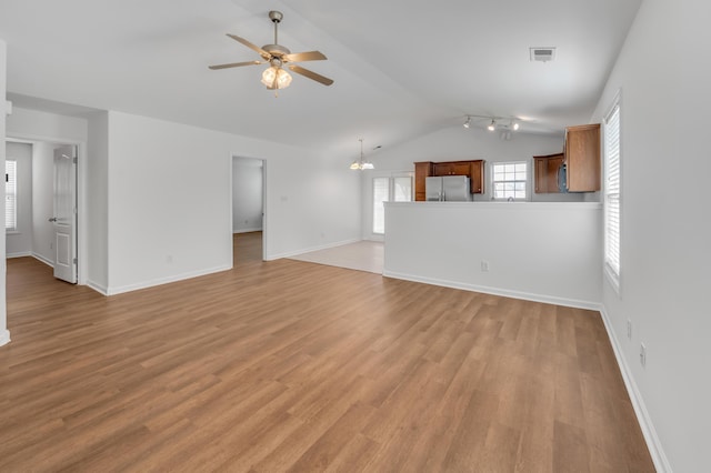 unfurnished living room featuring ceiling fan with notable chandelier, light wood-type flooring, visible vents, vaulted ceiling, and baseboards