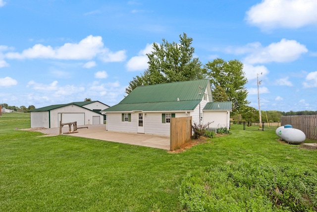 rear view of house featuring a lawn, a patio area, a detached garage, fence, and an outdoor structure