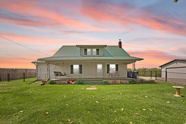 back of property at dusk with a lawn, fence, a chimney, and a porch