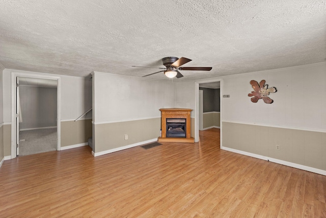 unfurnished living room with baseboards, ceiling fan, light wood-type flooring, and a textured ceiling