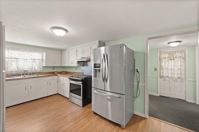 kitchen with baseboards, light wood-type flooring, under cabinet range hood, a sink, and appliances with stainless steel finishes