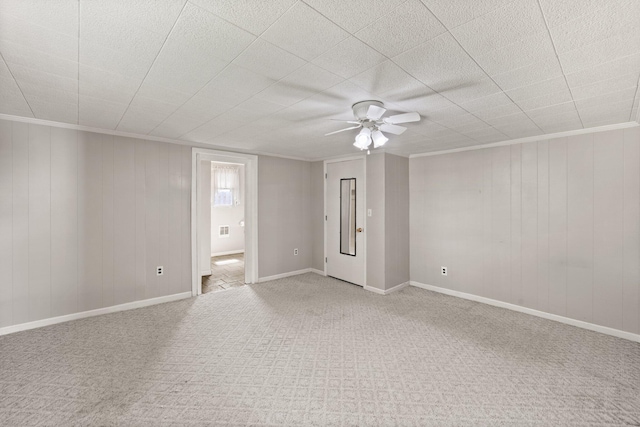 empty room with crown molding, a ceiling fan, wood walls, and light colored carpet