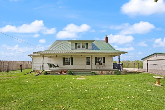 rear view of house featuring fence, a yard, a chimney, and metal roof
