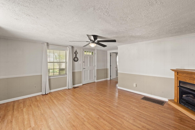 unfurnished living room featuring visible vents, wood finished floors, ceiling fan, a fireplace with raised hearth, and a textured ceiling
