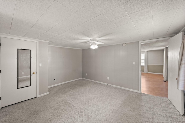below grade area with crown molding, baseboards, carpet, and a ceiling fan