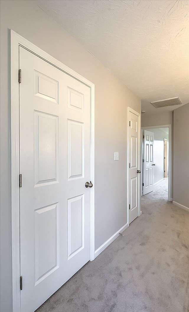 corridor featuring baseboards, visible vents, and light colored carpet