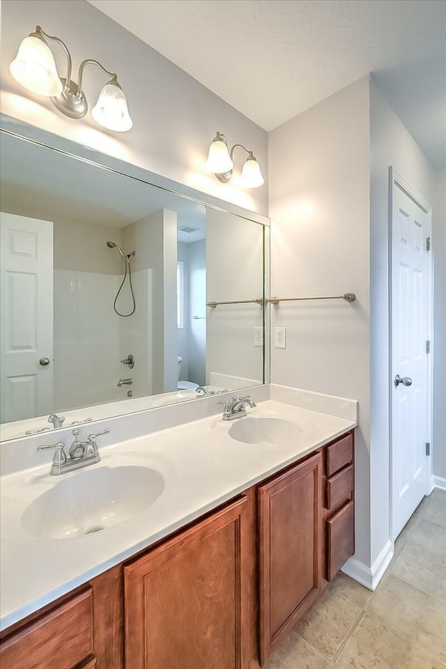 bathroom featuring toilet, a sink, double vanity, and baseboards