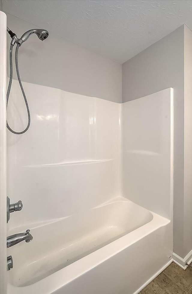 full bath featuring baseboards, a textured ceiling, and bathing tub / shower combination