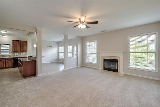unfurnished living room with a high end fireplace, a wealth of natural light, baseboards, and ceiling fan with notable chandelier
