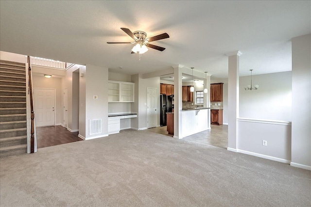 unfurnished living room featuring ceiling fan with notable chandelier, baseboards, visible vents, and carpet floors