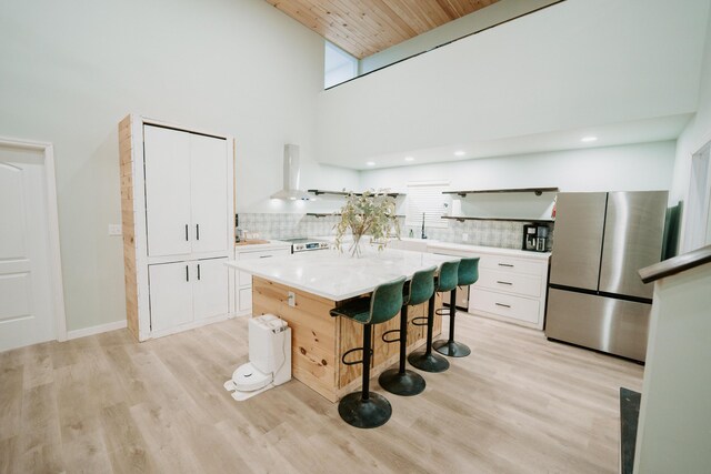 kitchen with a breakfast bar area, white cabinetry, a high ceiling, range hood, and freestanding refrigerator