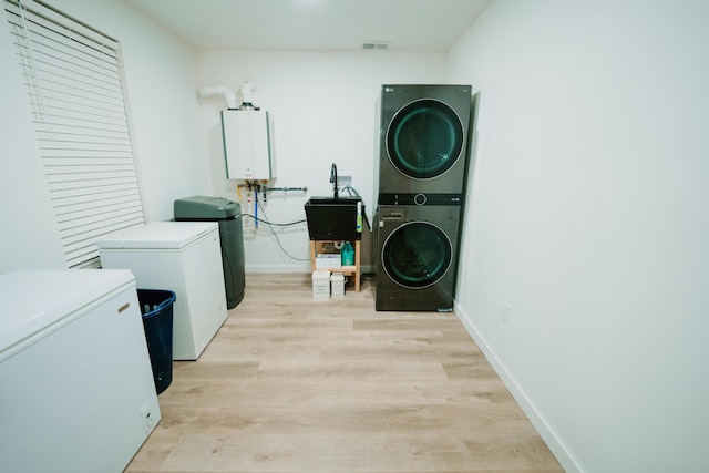 laundry area with light wood finished floors, visible vents, stacked washer / dryer, water heater, and laundry area