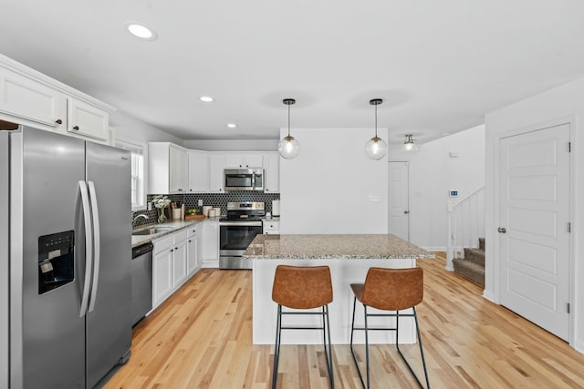 kitchen with white cabinets, stainless steel appliances, light wood-type flooring, and a kitchen island
