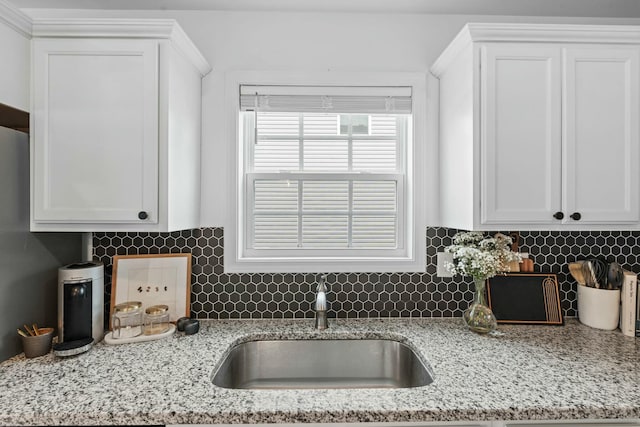 kitchen with light stone counters, white cabinets, tasteful backsplash, and a sink