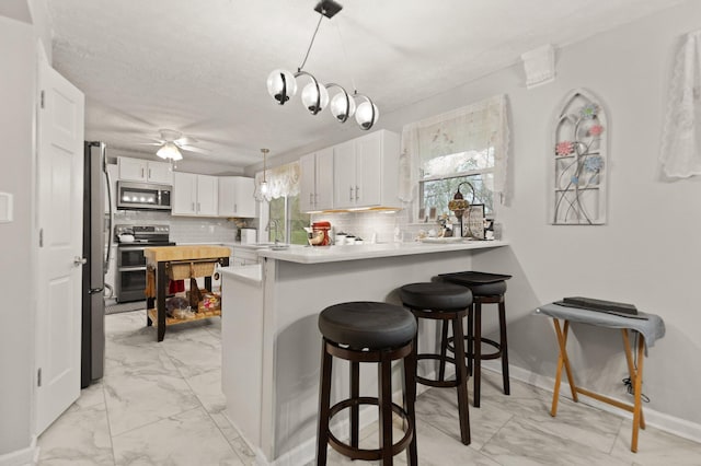kitchen featuring a ceiling fan, decorative backsplash, marble finish floor, stainless steel appliances, and a peninsula
