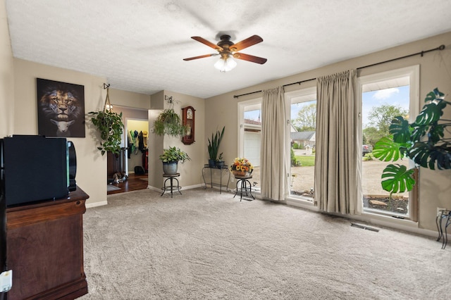 living area featuring a textured ceiling, ceiling fan, baseboards, carpet flooring, and visible vents