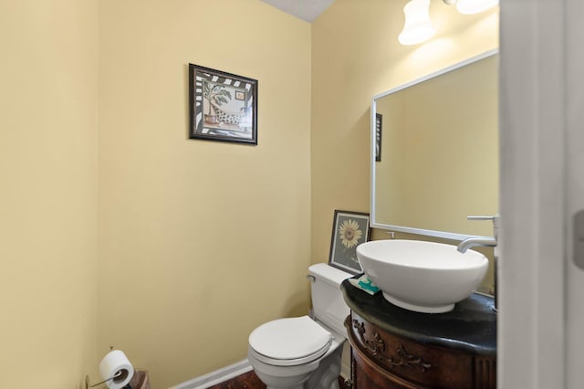 half bathroom with baseboards, wood finished floors, toilet, and vanity