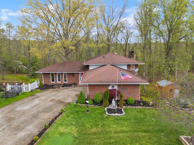 view of front of house with a front lawn, driveway, a chimney, brick siding, and a view of trees