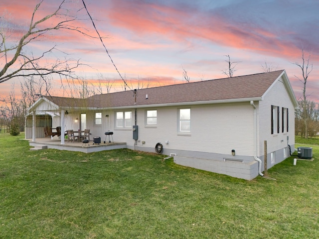 back of property at dusk with a yard, a patio area, and central AC