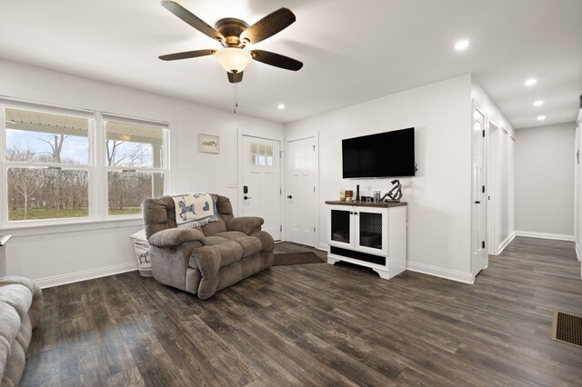 living room with dark wood-type flooring, visible vents, a ceiling fan, and baseboards