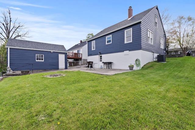 rear view of property with central AC unit, a chimney, a patio area, a shingled roof, and a yard