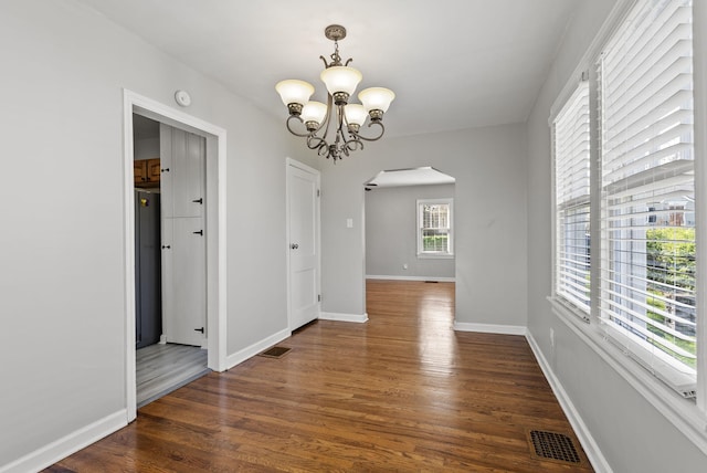 unfurnished dining area with arched walkways, baseboards, an inviting chandelier, visible vents, and dark wood-type flooring
